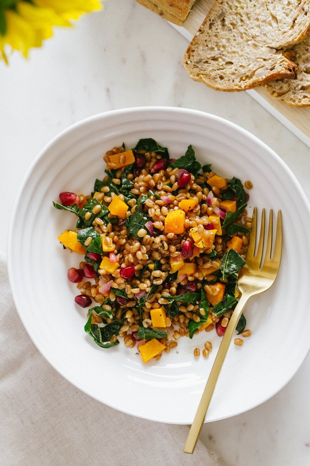 top down view of a serving of autumn wheat berry and butternut squash salad in a white bowl with gold fork.