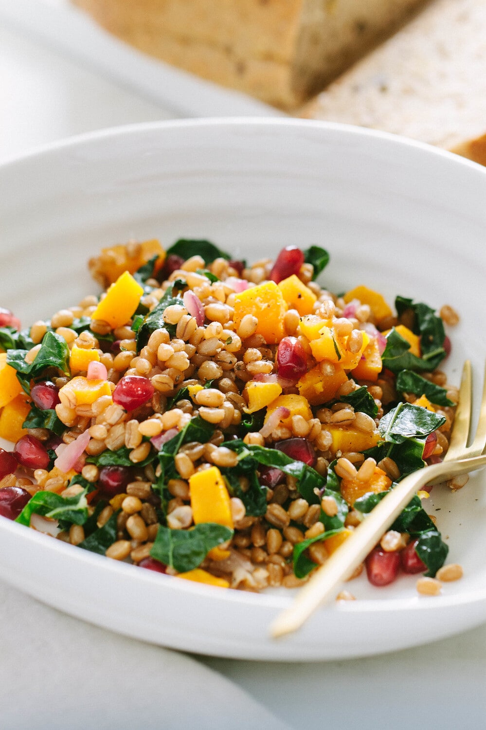 side angle view of a serving of autumn wheat berry and butternut squash salad in a white bowl with gold fork.