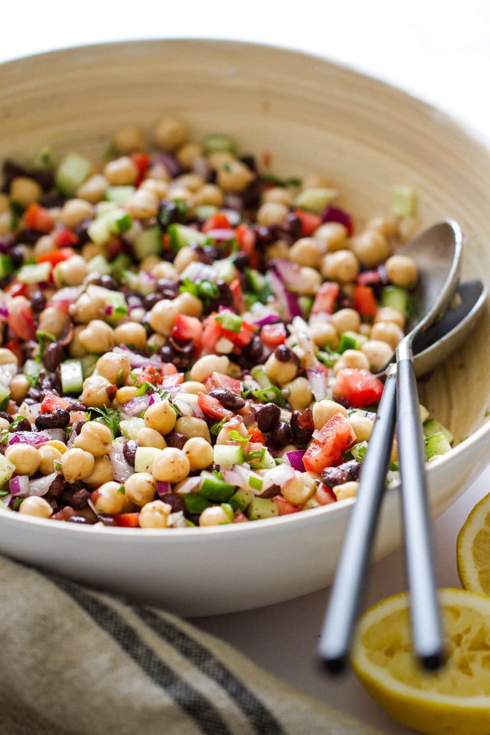 a side angle view of balela salad in a white serving bowl with silver utensils with black handles