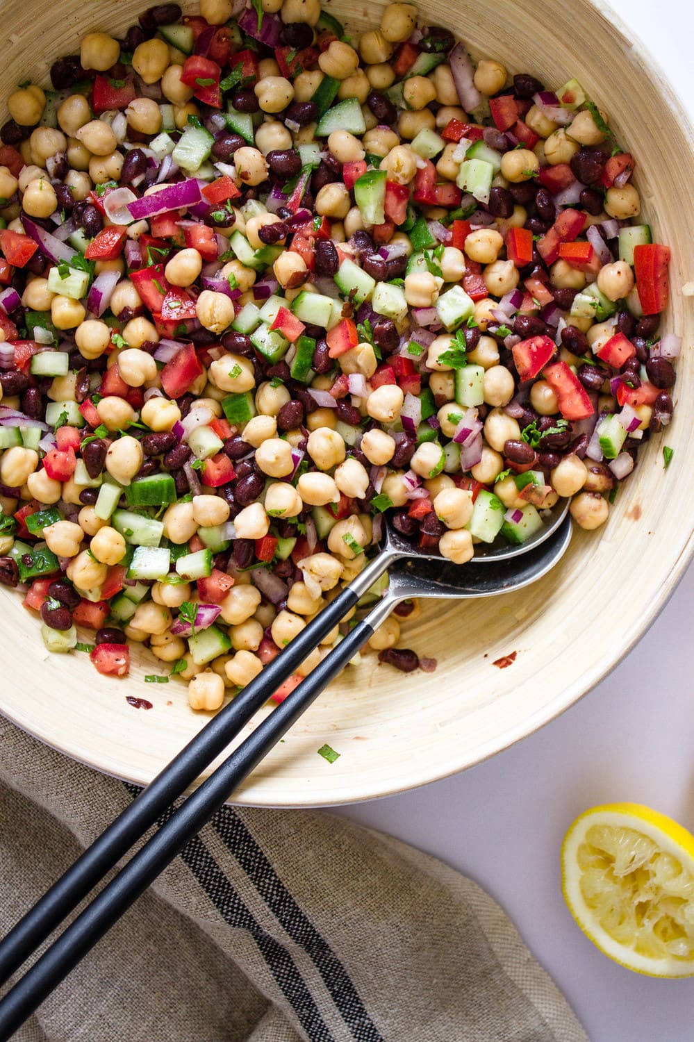 top down view of balela salad just mixed together in a large bamboo mixing bowl with silver utensils with black handles