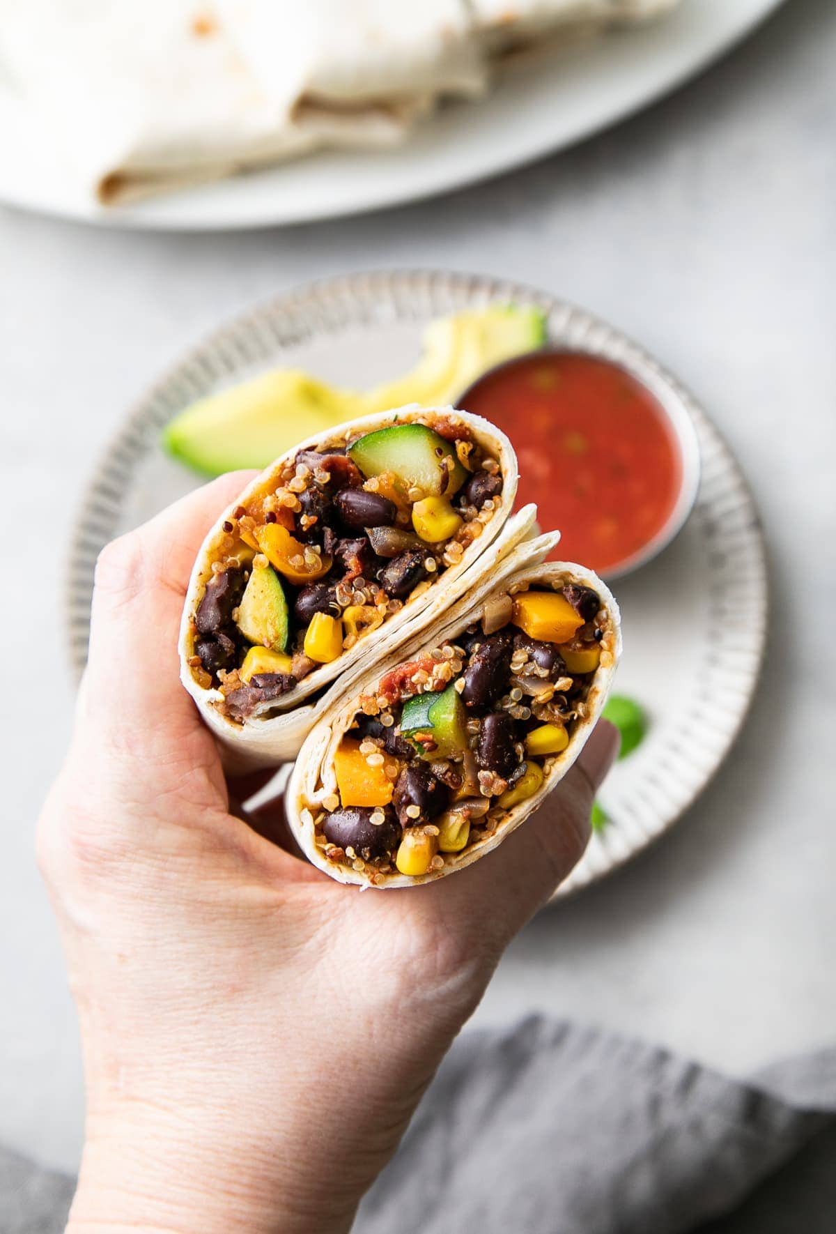 top down view of hand holding a black bean quinoa burrito sliced in half.