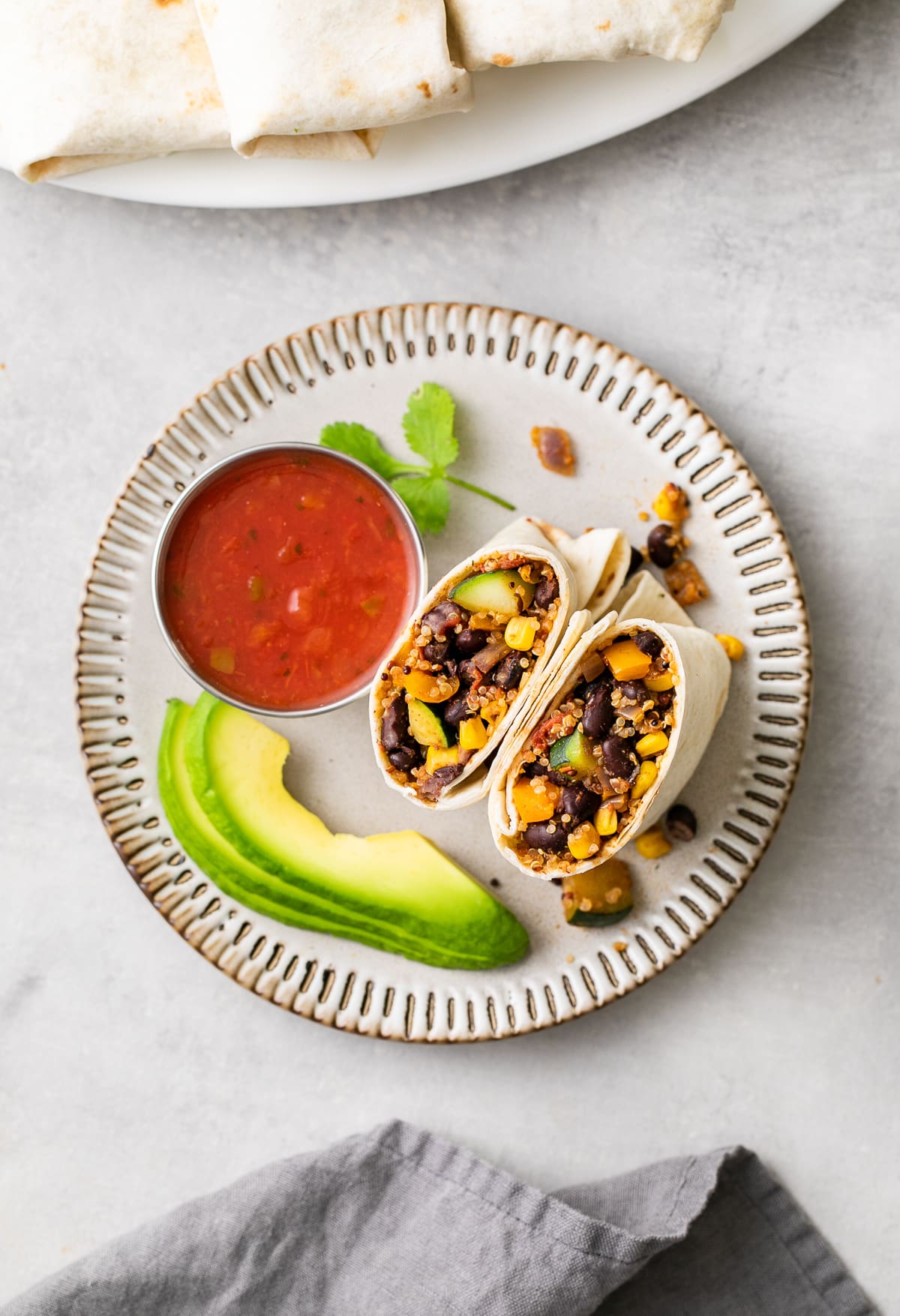 top down view of plate with vegan burrito sliced in half with items surrounding.