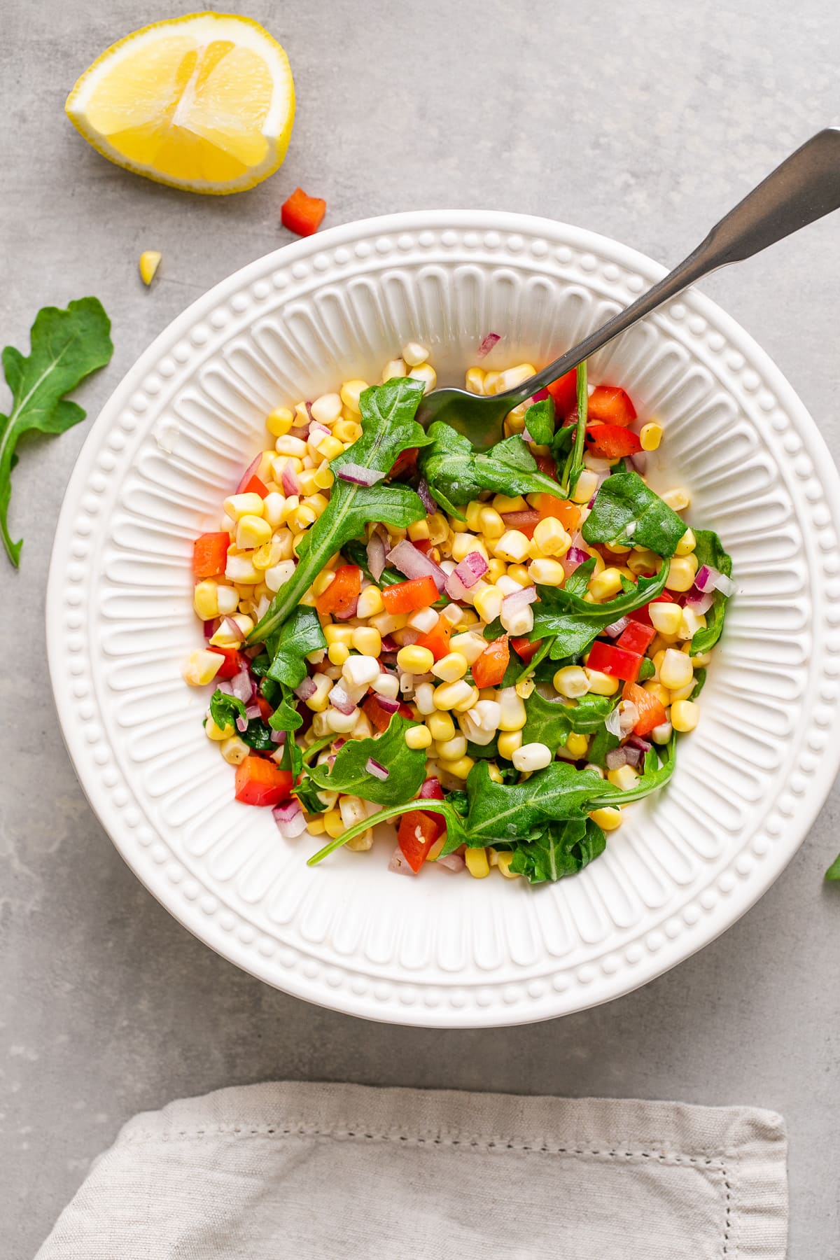 top down view of bowl with serving of corn arugula salad with items surrounding.
