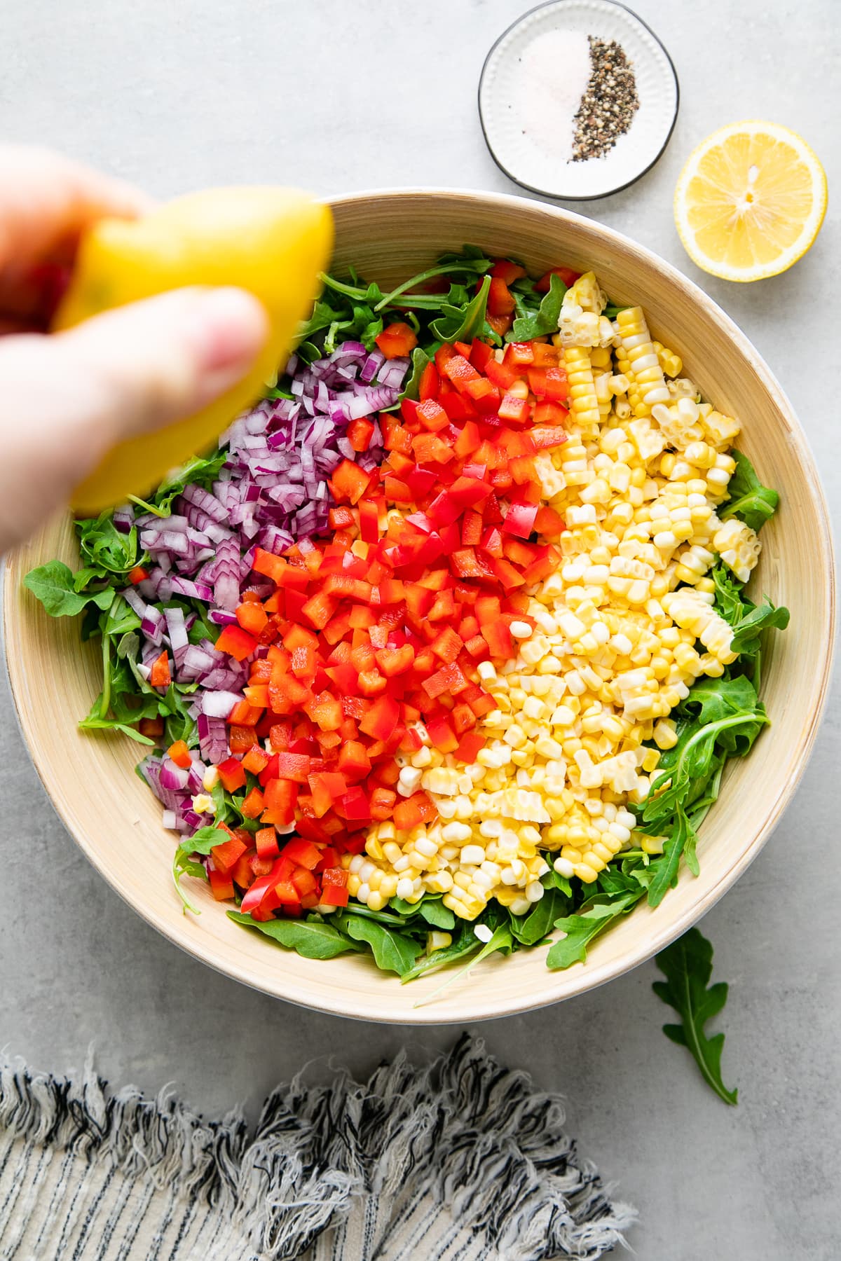 top down view of bowl with corn arugula salad ingredients added and lemon drizzled over top.