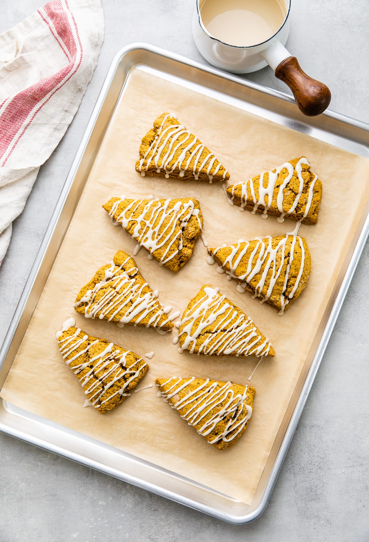 top down view of pumpkin scones with maple glaze on baking sheet with items surrounding.