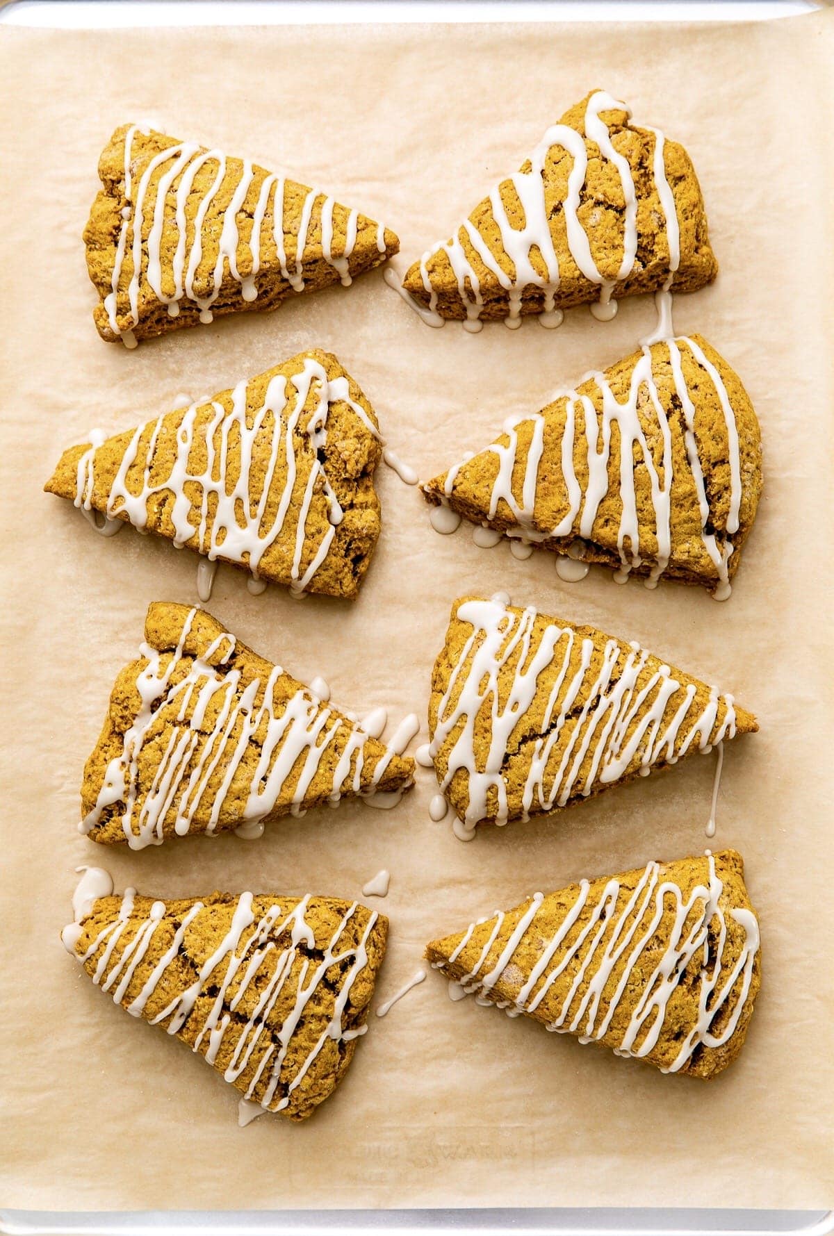 top down view of pumpkin scones with maple glaze on baking sheet.