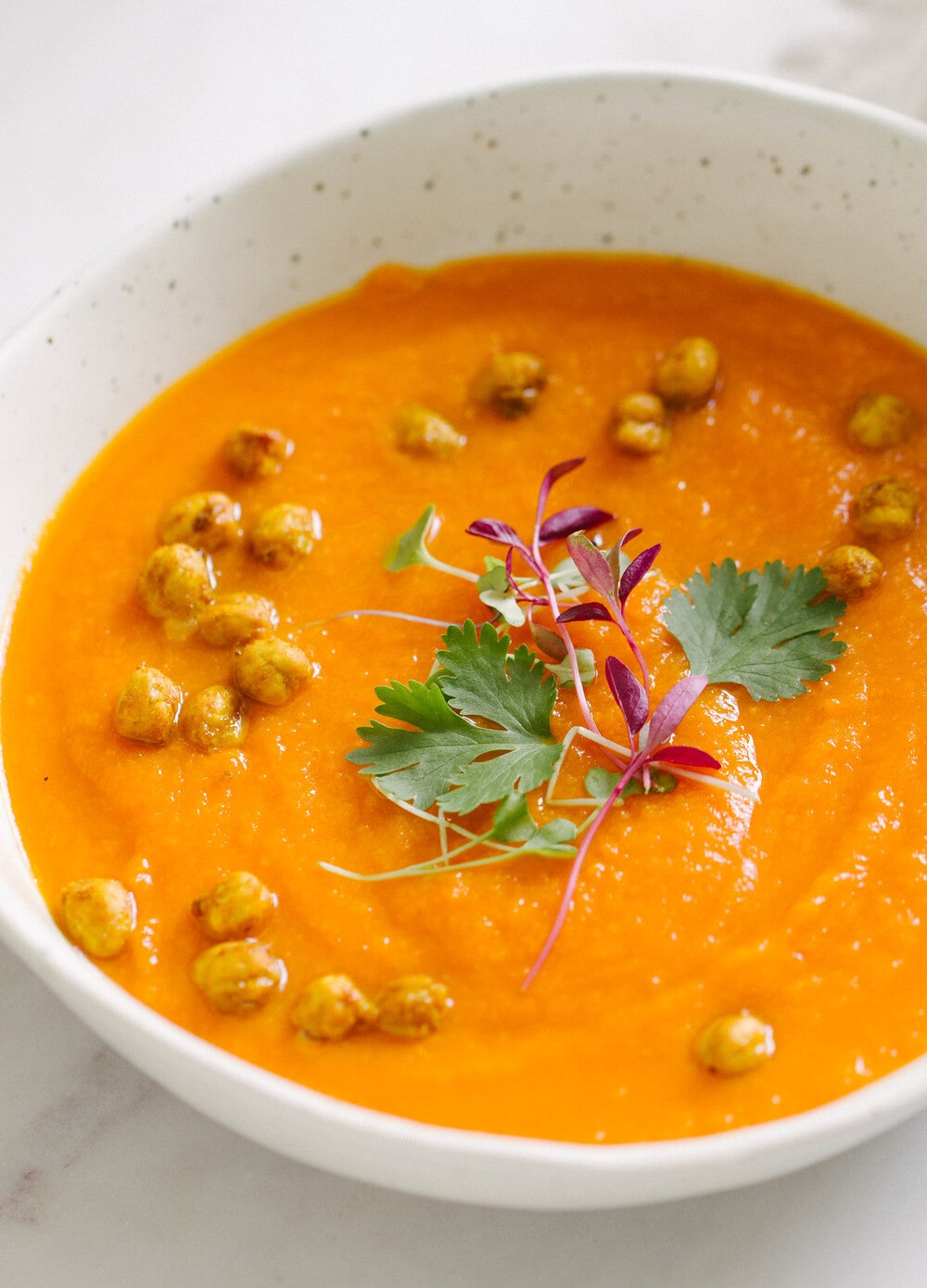 side angle view of carrot sweet potato coriander soup with turmeric roasted chickpeas in a bowl.