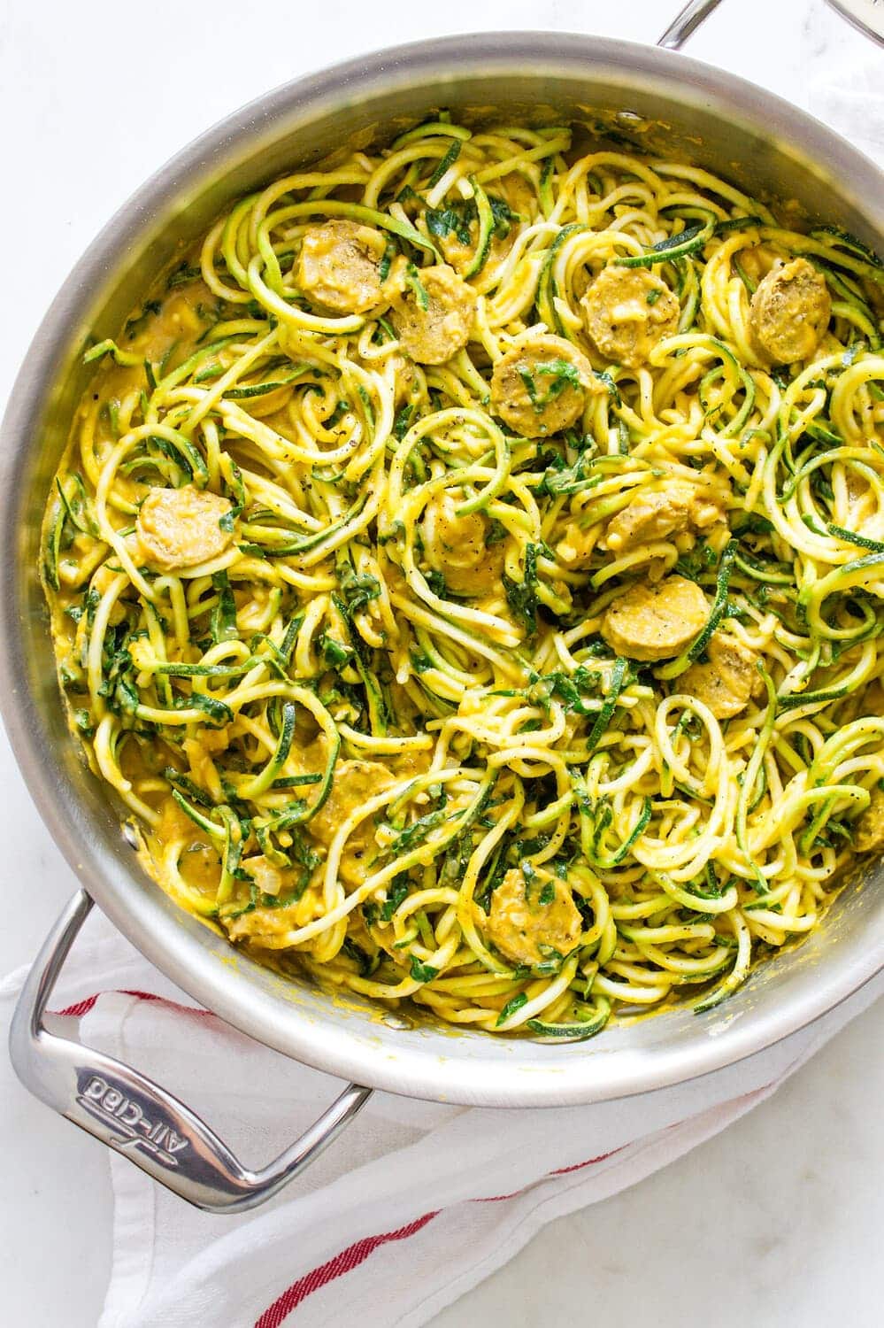 top down view of a pan with cooked zucchini noodles tossed with creamy pumpkin sauce, kale and mushrooms.