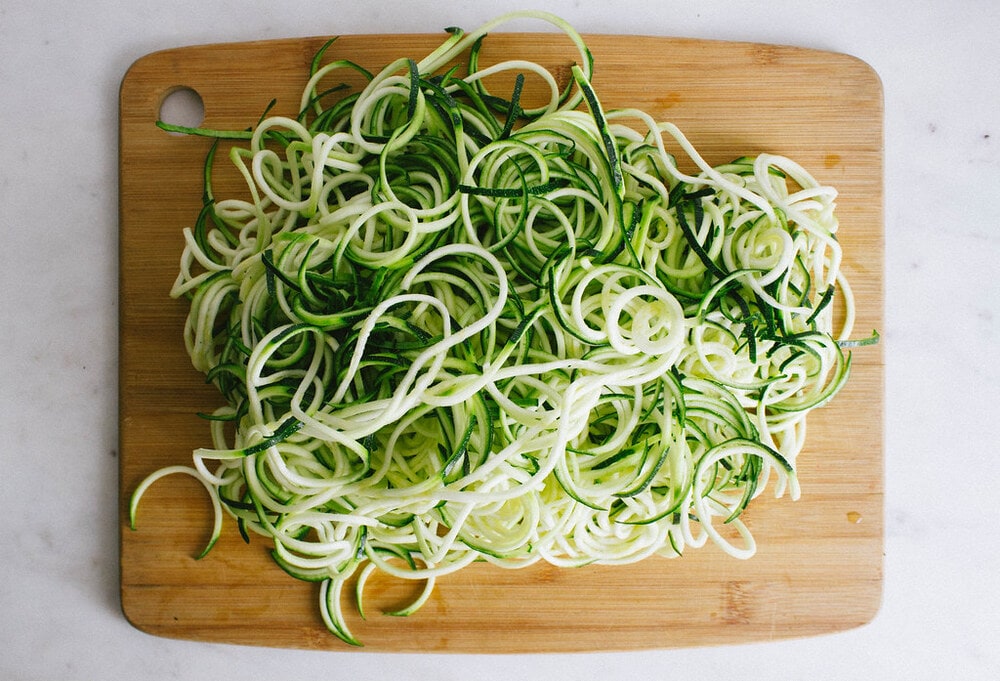 top down view of spiralized zucchini noodles on a wooden cutting board.