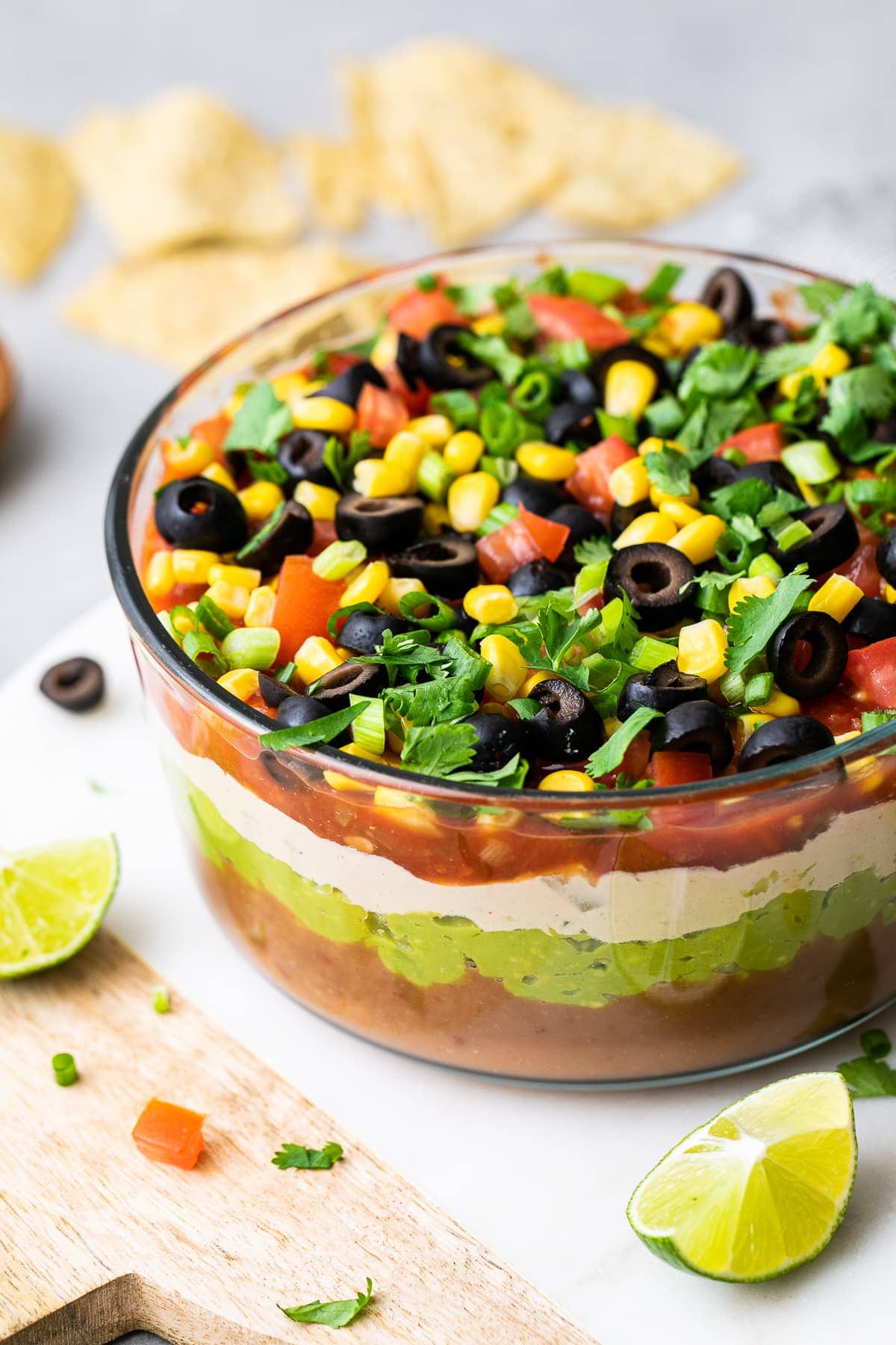 side angle view of vegan seven layer dip in glass bowl with items surrounding.