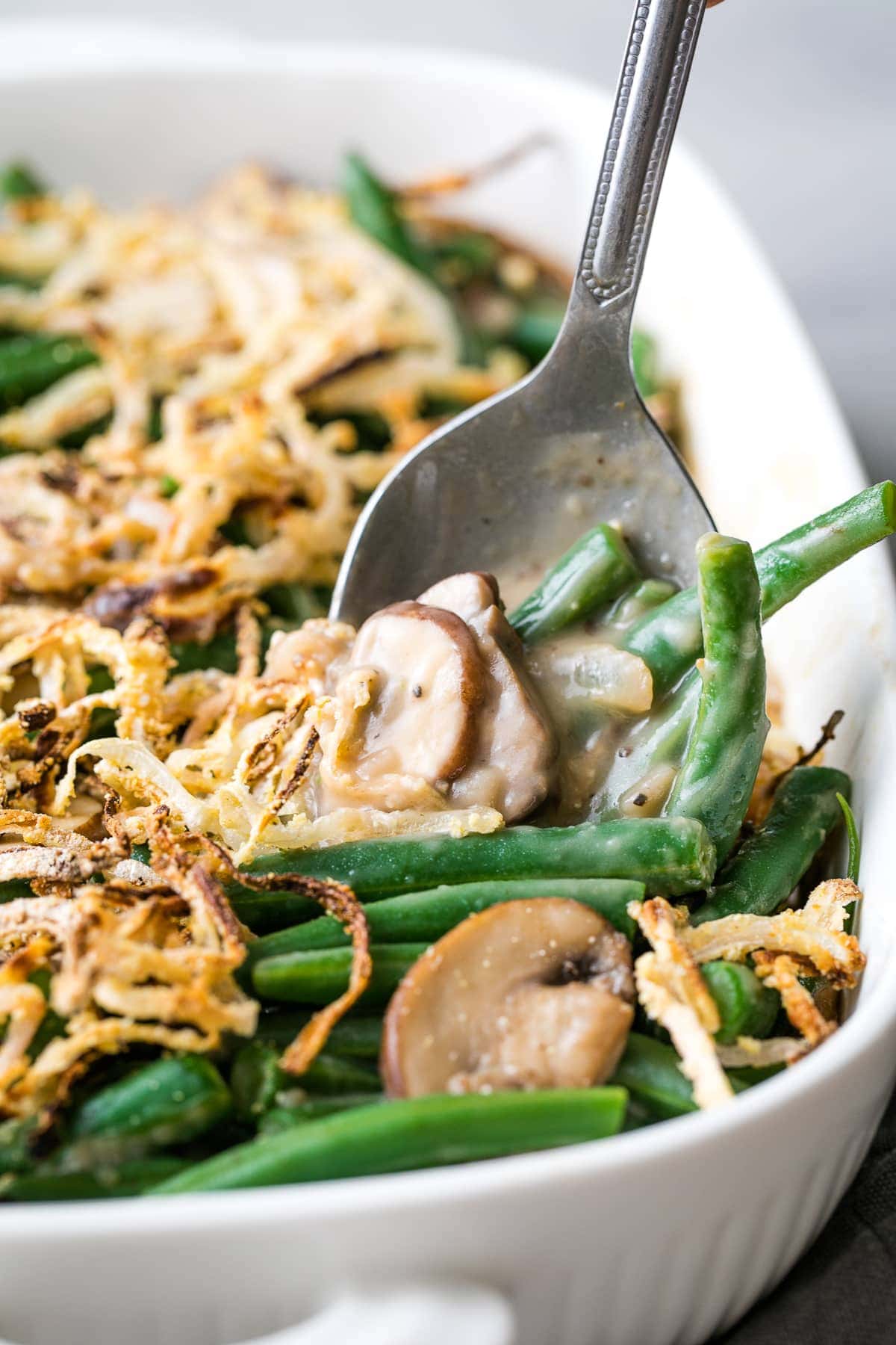 head on view of spoon scooping up vegan green bean casserole in a baking dish.