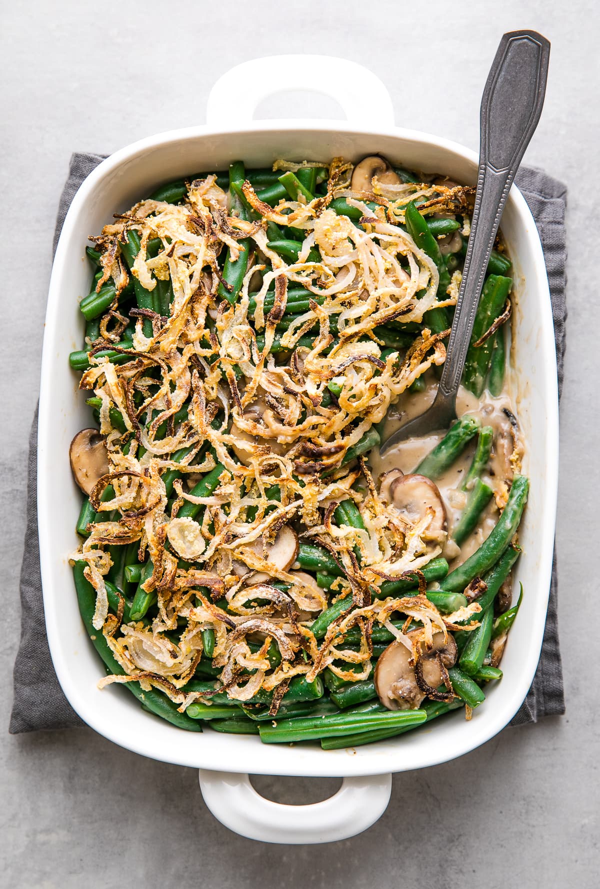 top down view of freshly baked vegan green bean casserole in a white baking dish with serving spoon.