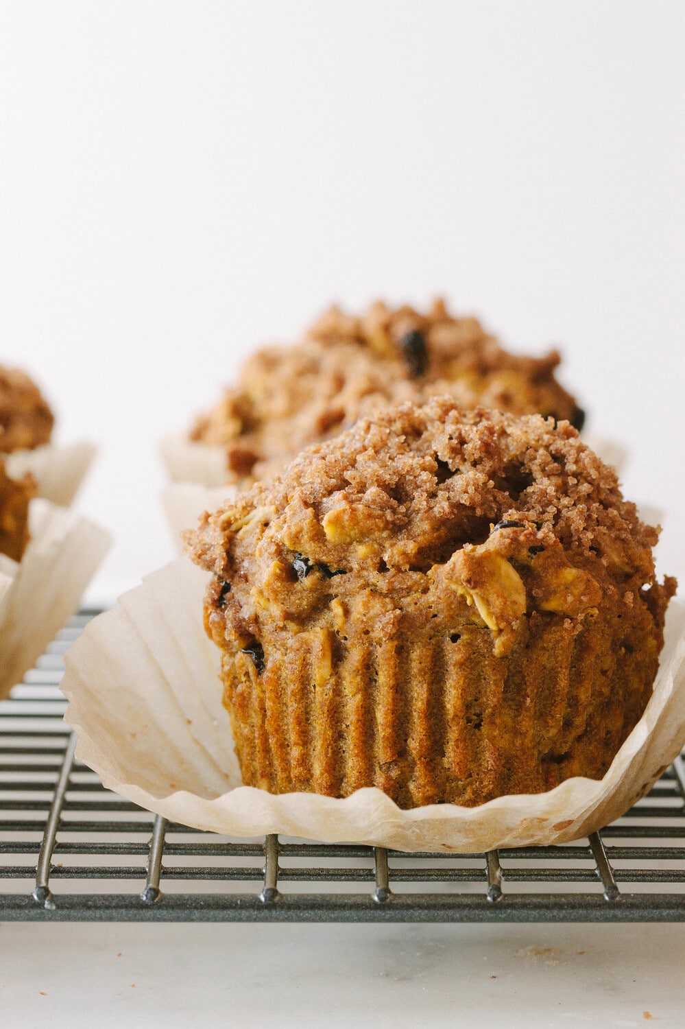 head on shot of vegan pumpkin muffin on a wire rack with liner pulled away from the muffin.