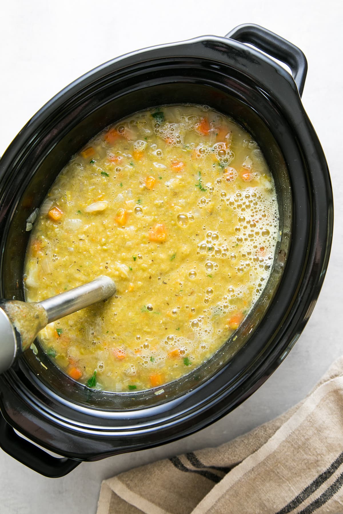 top down view showing the process of pureeing split pea soup in a slow cooker.