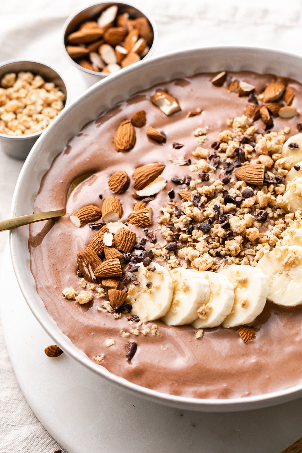 side angle view of chocolate almond butter smoothie in a bowl with items surrounding.