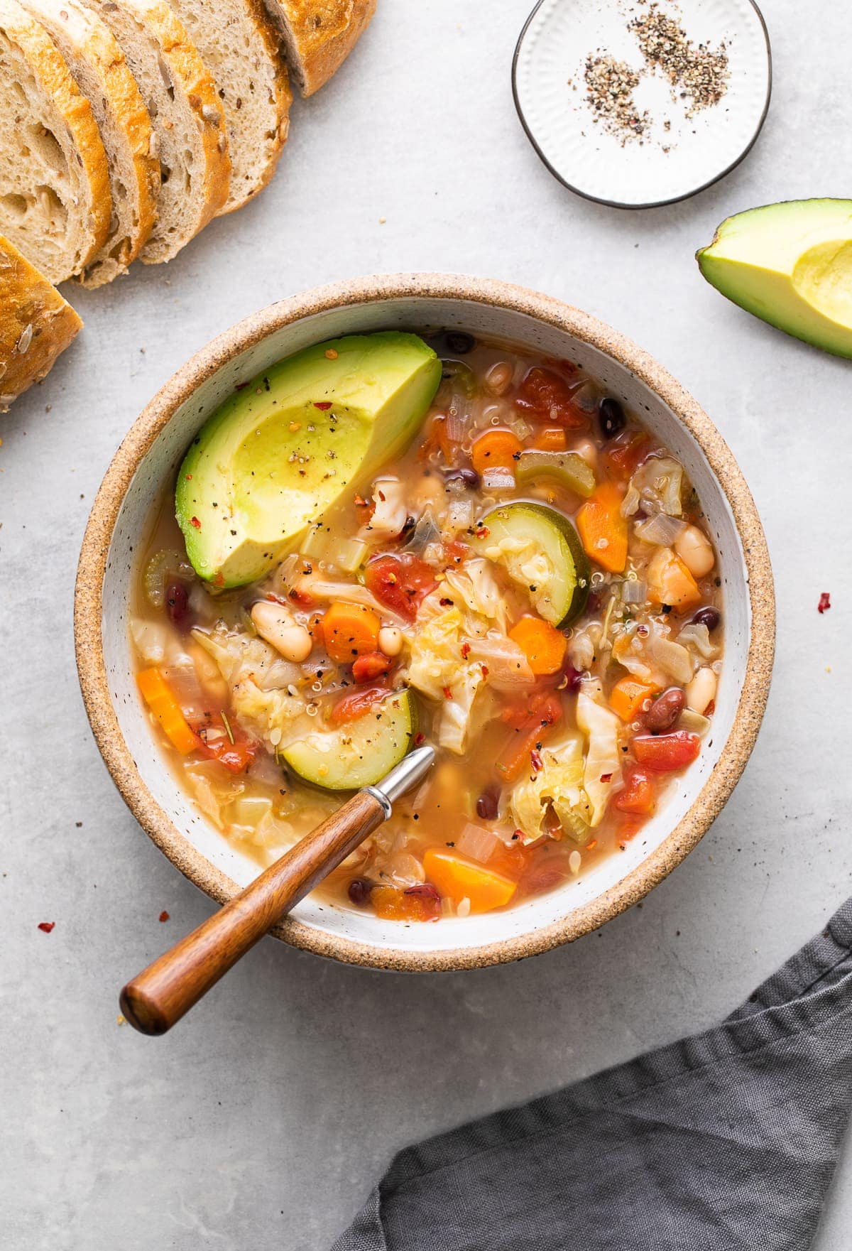 top down view of bowl of vegetable quinoa soup with spoon and items surrounding.