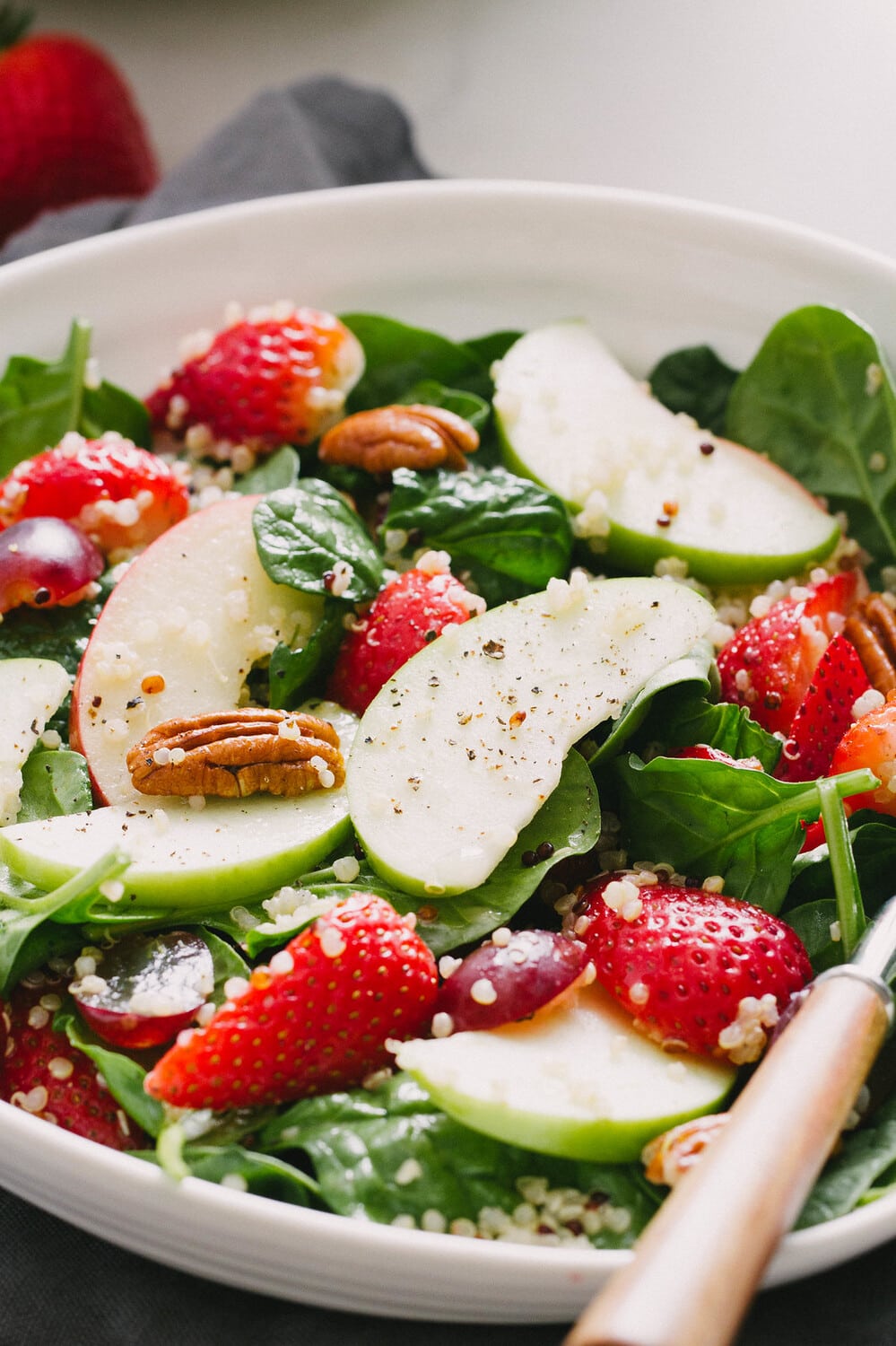 side angle view of spinach salad with strawberries, apples and quinoa.