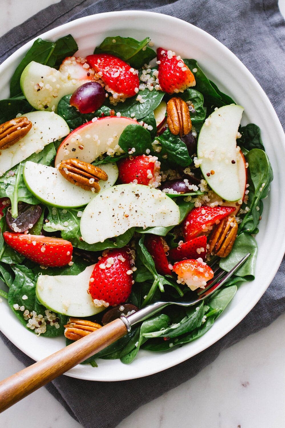top down view of a spinach salad with strawberries, apples and quinoa in a serving bowl.