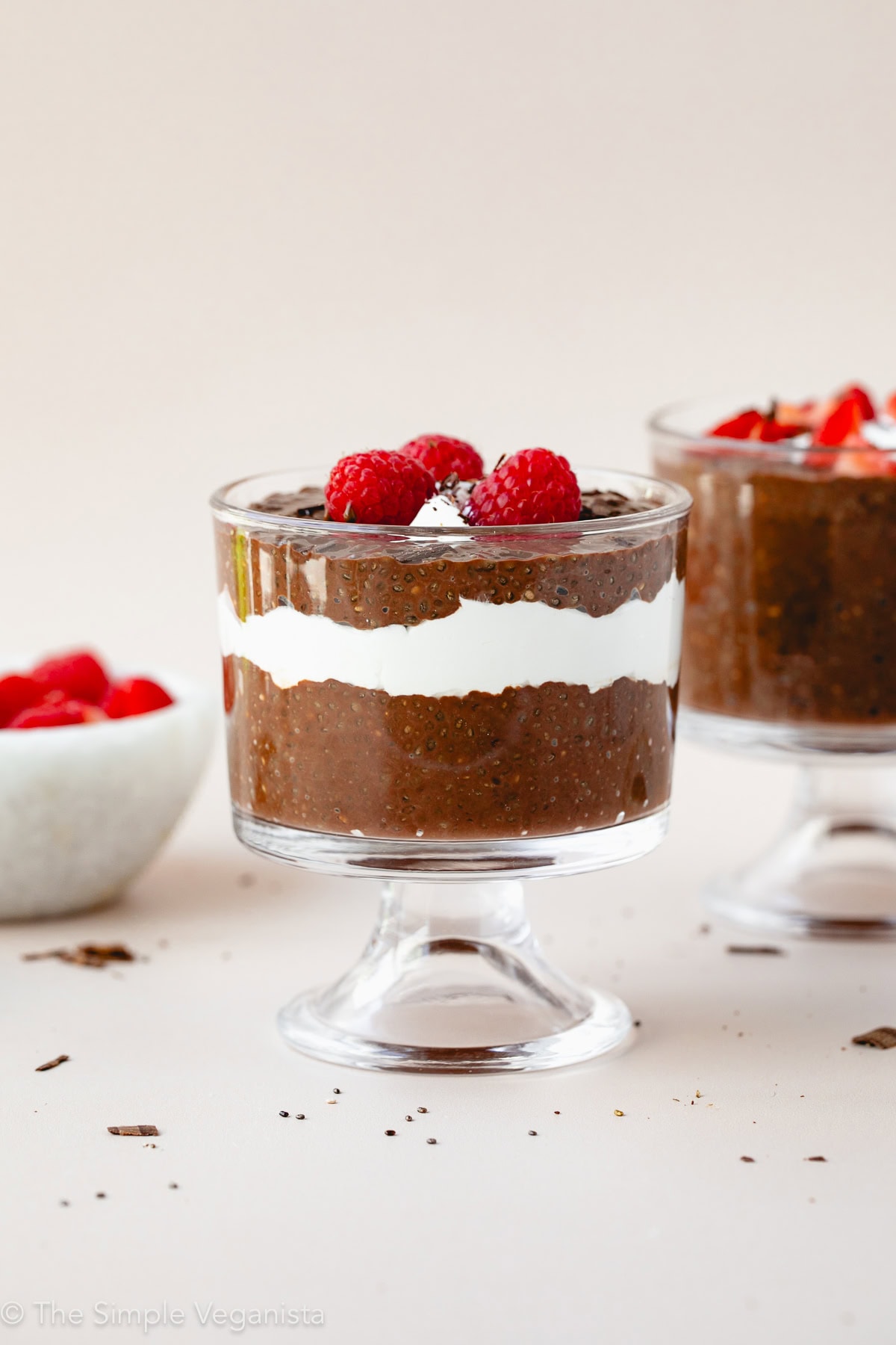 head on view of chocolate chia pudding in a glass with toppings and items surrounding.