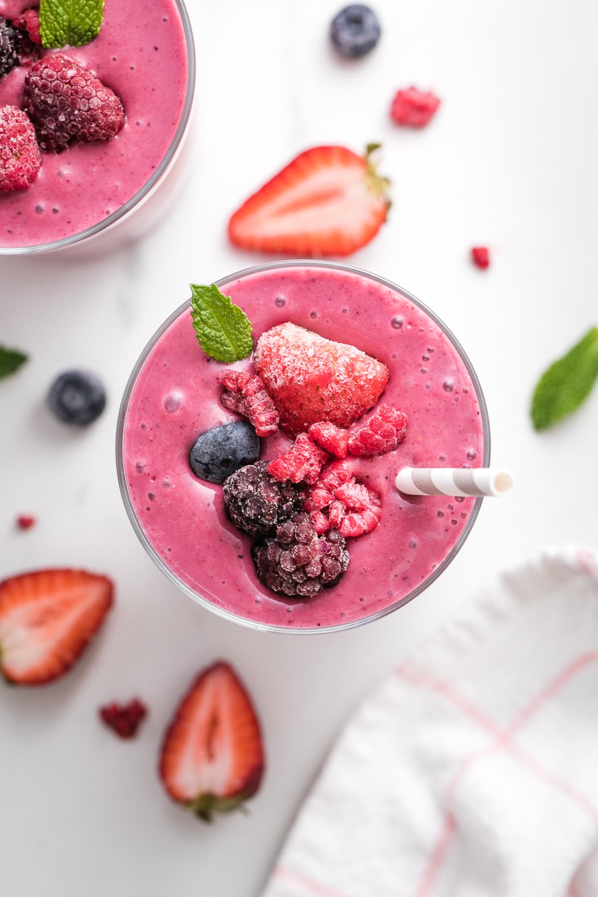 top down view of healthy mixed berry yogurt smoothie in a glass with straw and items surrounding.