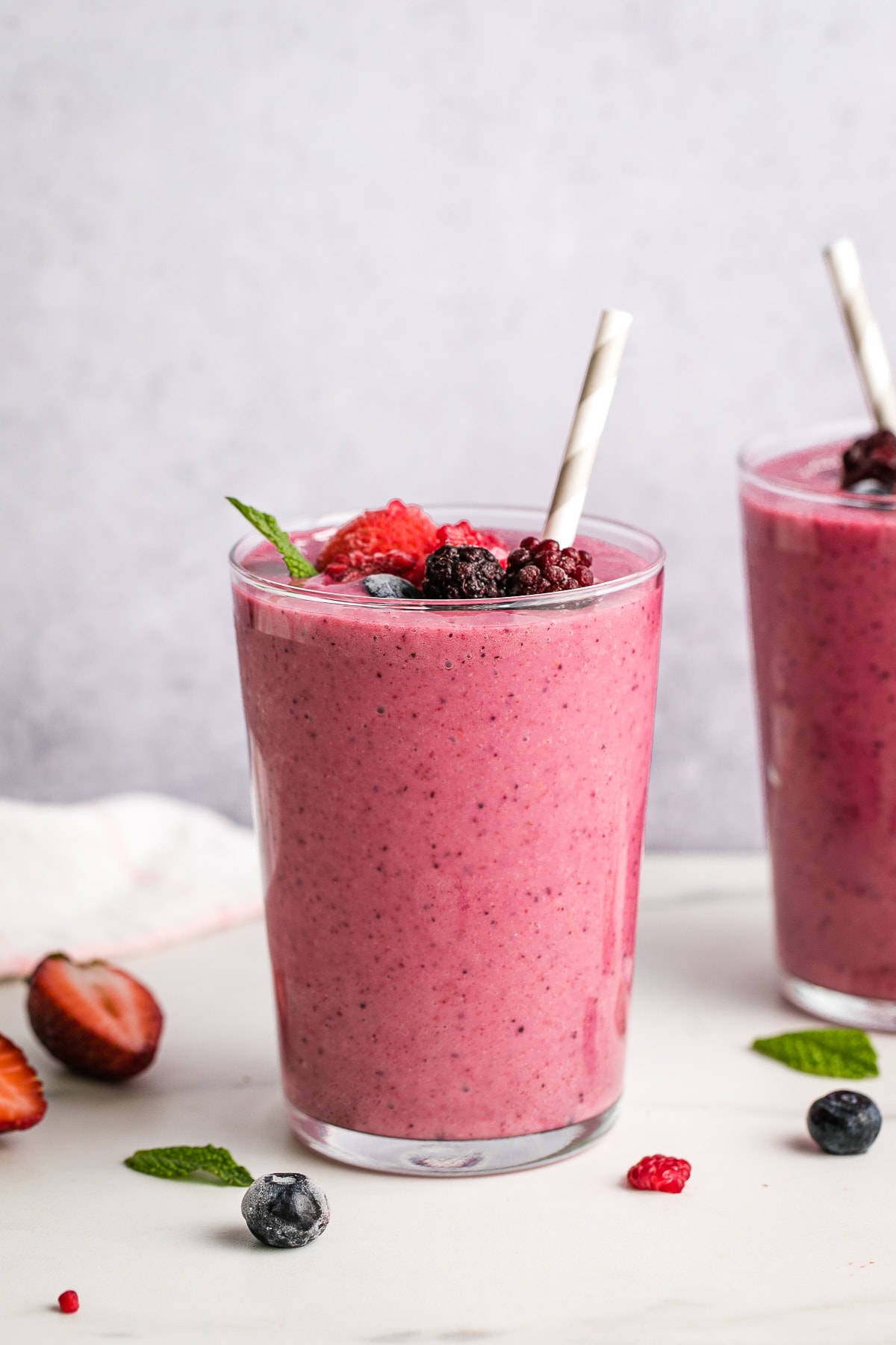 head on view of healthy mixed berry yogurt smoothie in a glass with straw and items surrounding.