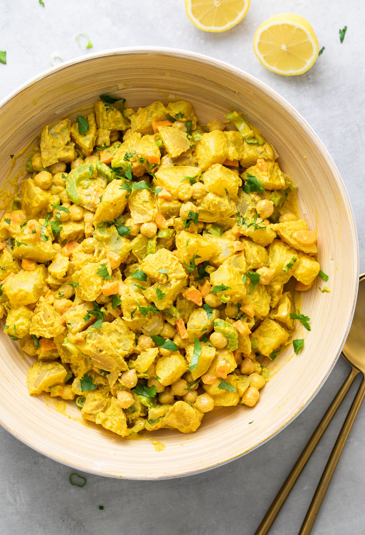 top down view of freshly made vegan curried potato salad in a large bowl with items surrounding.