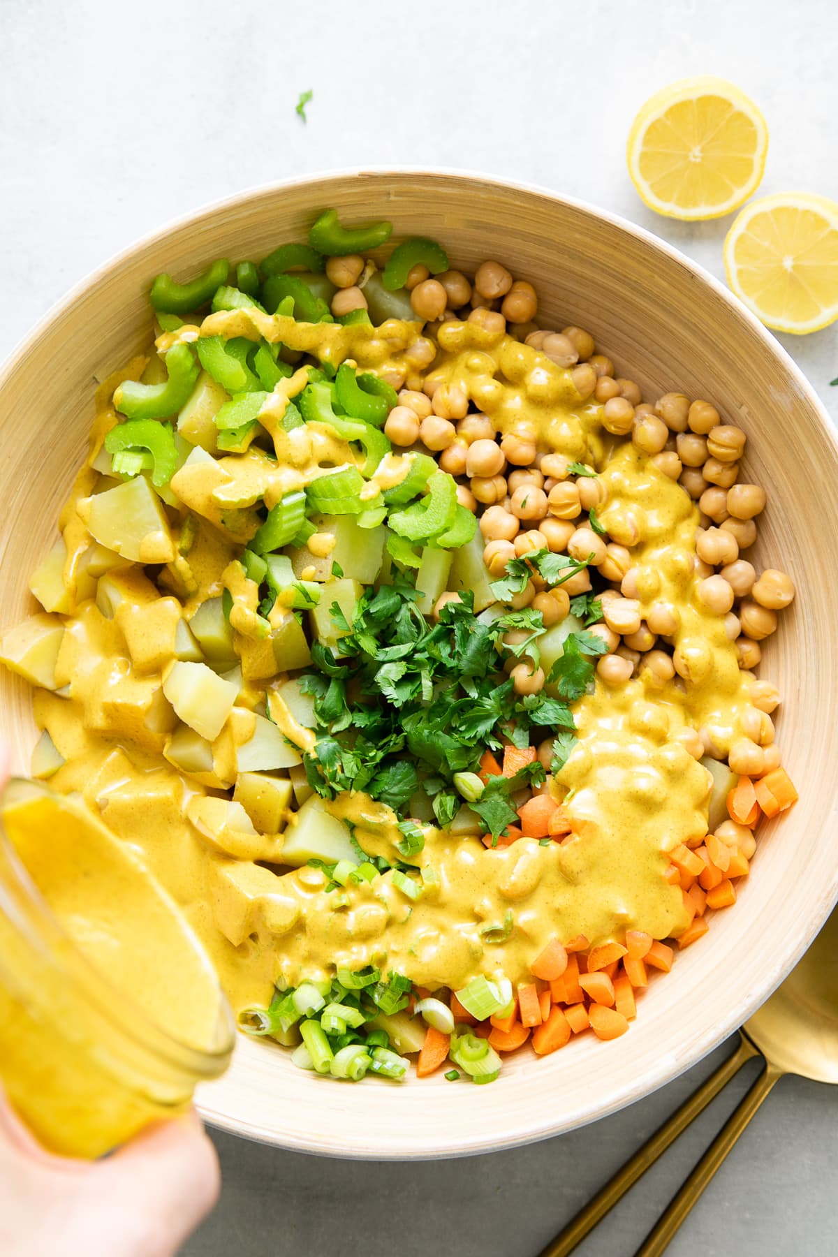 top down view of curried potato salad dressing being poured overtop potato salad ingredients.