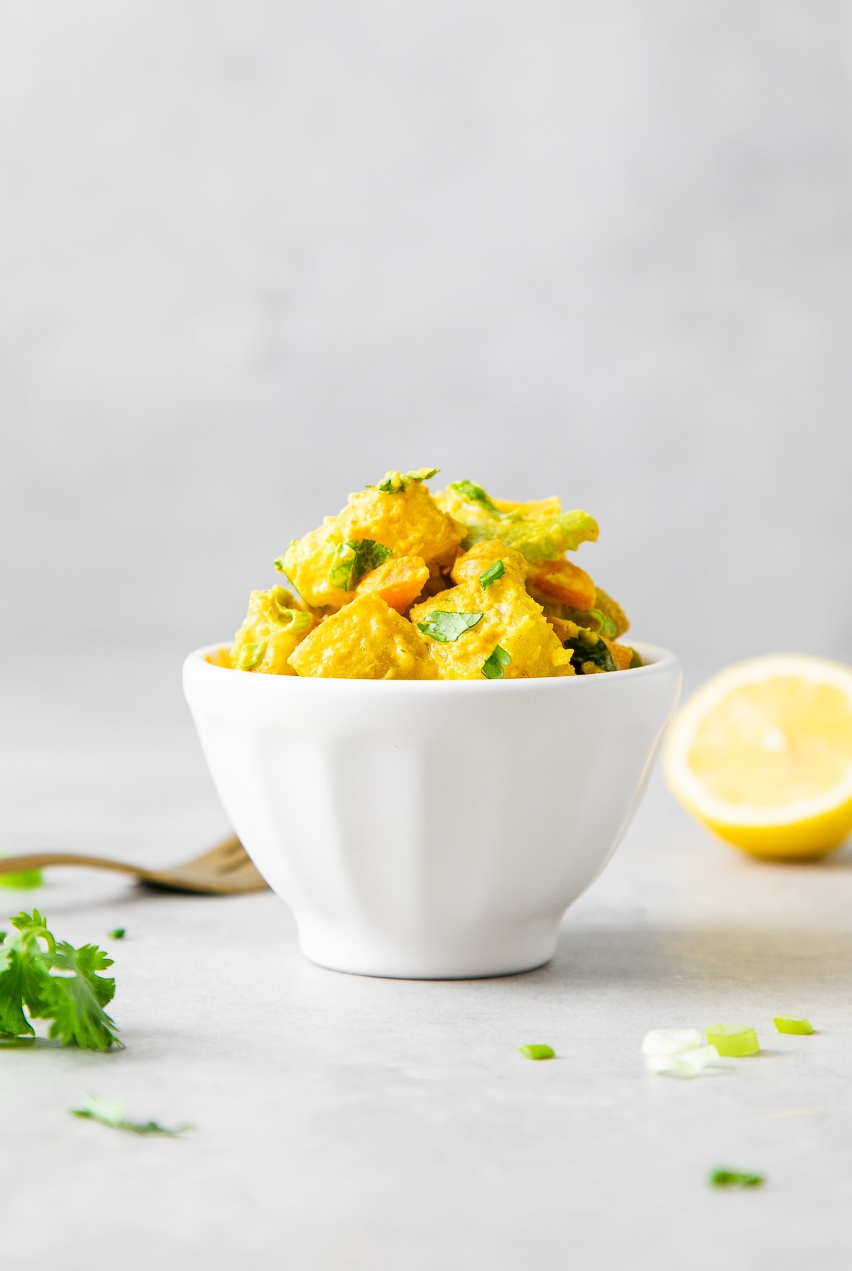 head on view of healthy curried potato salad in a small white bowl with items surrounding.