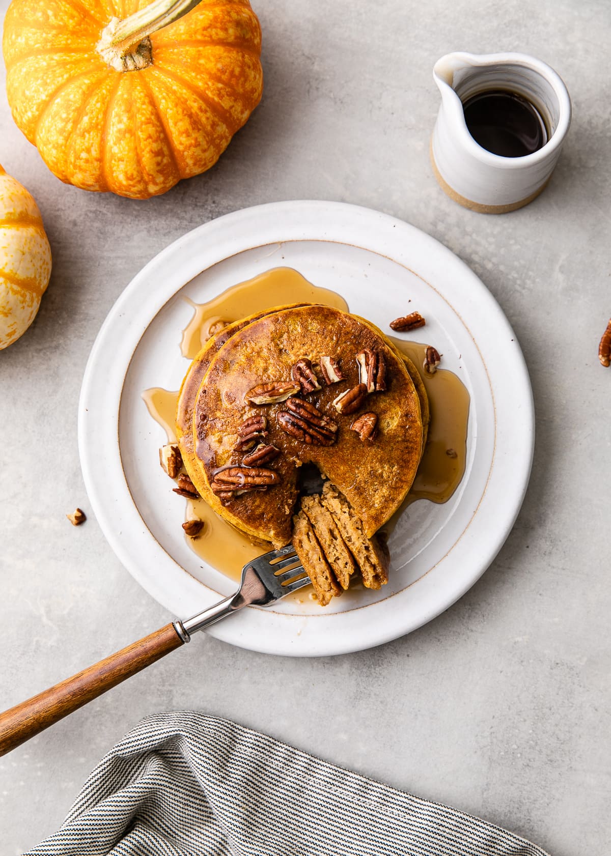 top down view of plate with pumpkin pancakes with bite on a fork and items surrounding.