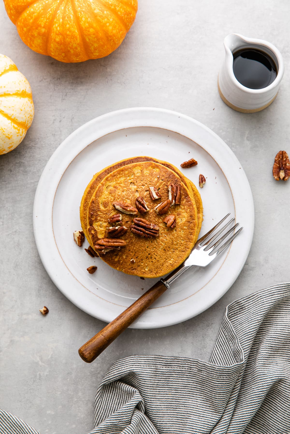 top down view of freshly made pumpkin pancakes on a plate with fork and items surrounding.