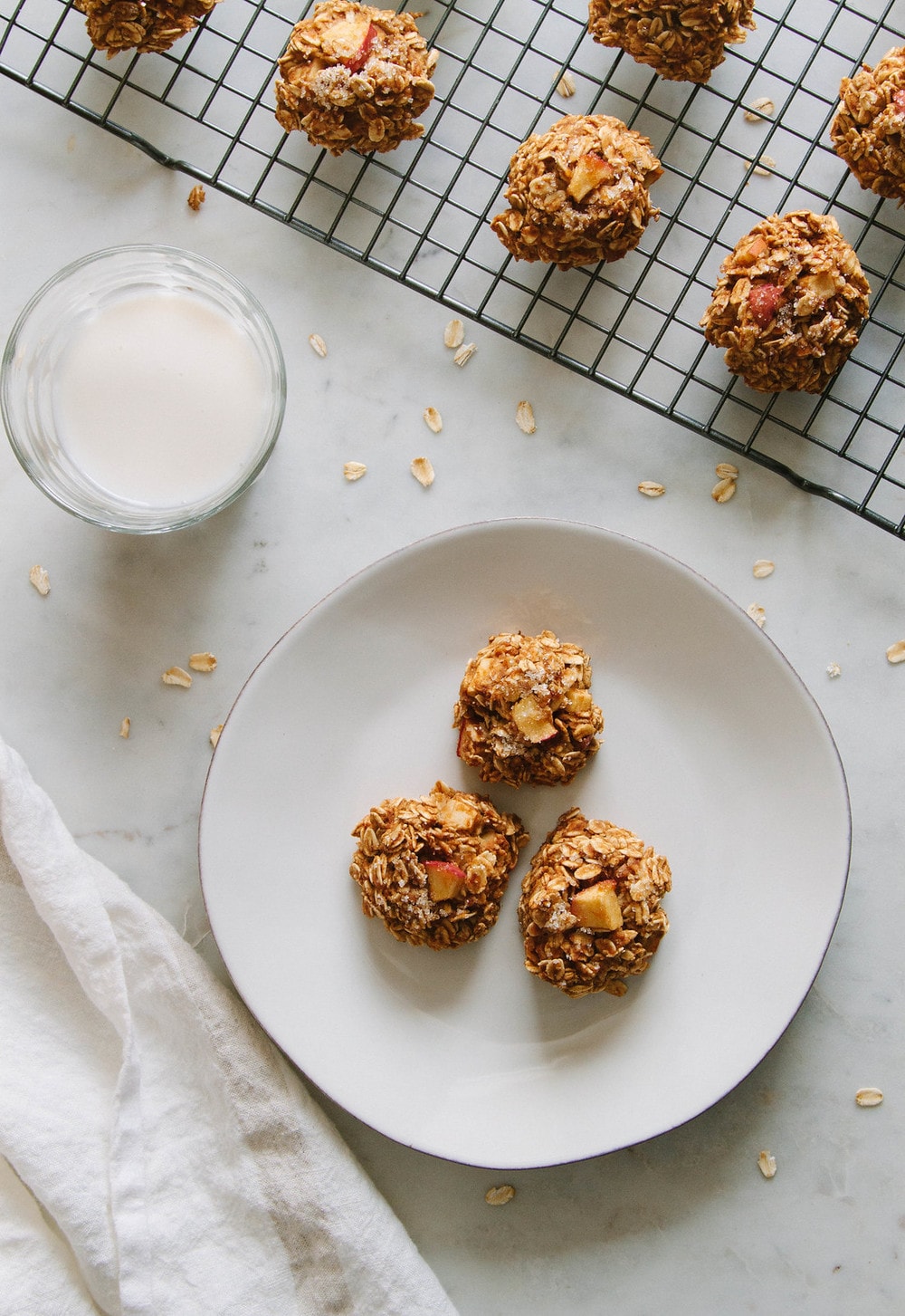 a top down view of three apple cinnamon oatmeal breakfast cookies on a white plate with glass of non-dairy milk