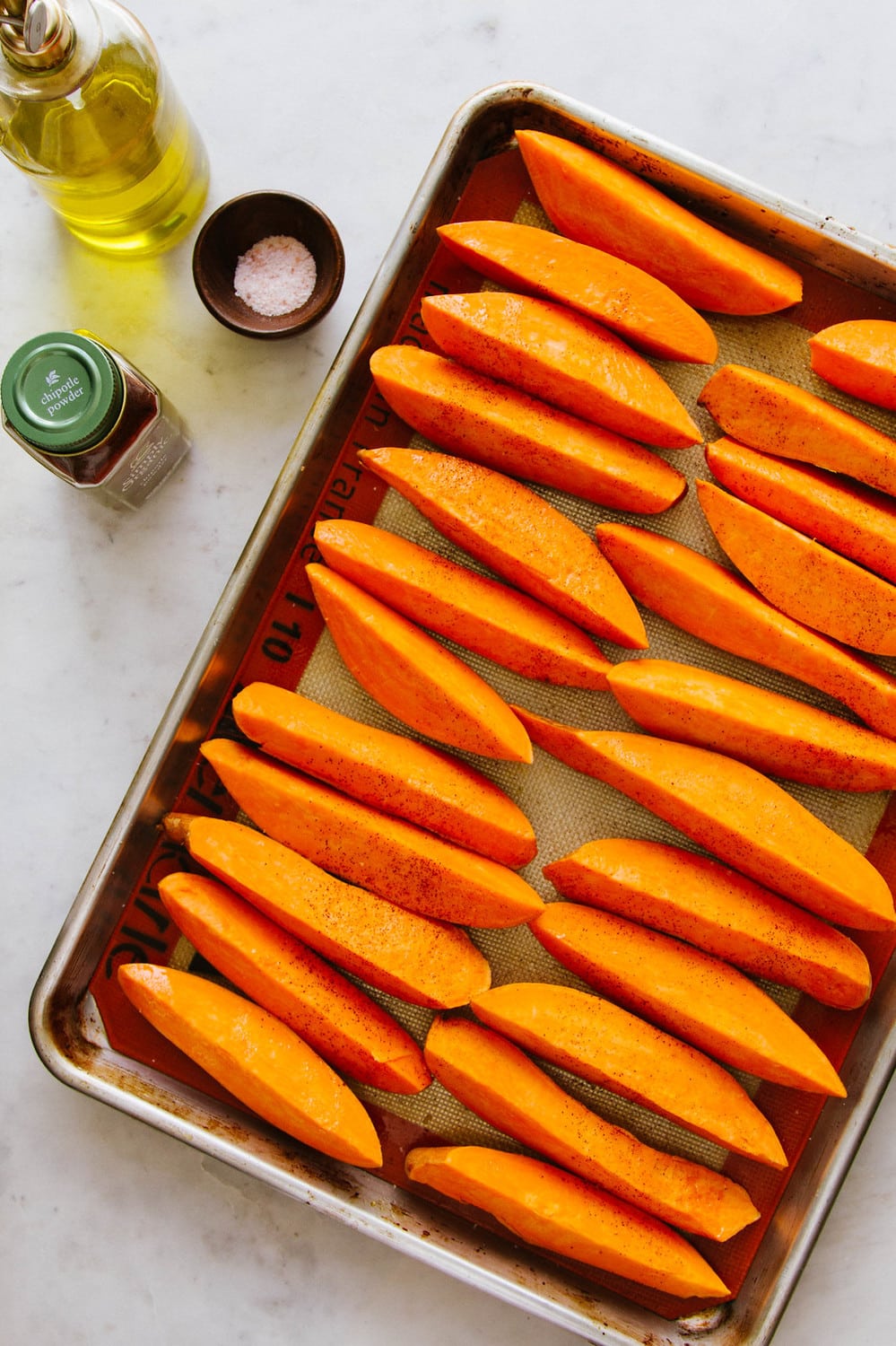 top down view of rimmed baking sheet with cut sweet potato wedges in a single layer