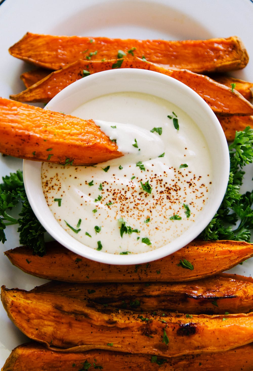 top down view, close up, of baked sweet potato wedge dipping into bowl of aioli