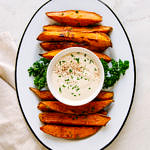 top down view of baked sweet potato wedges and aioli in a small bowl on an oval white plate with black rim