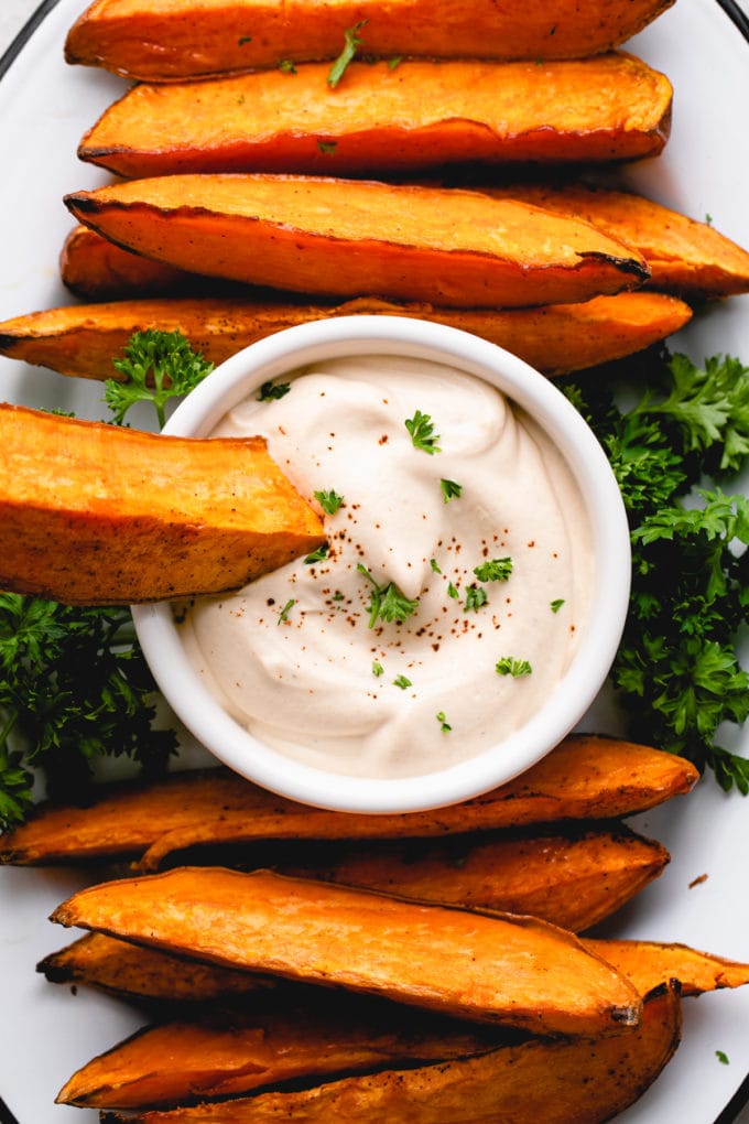 top down view of baked sweet potato wedge on a platter and dipped in to aioli.