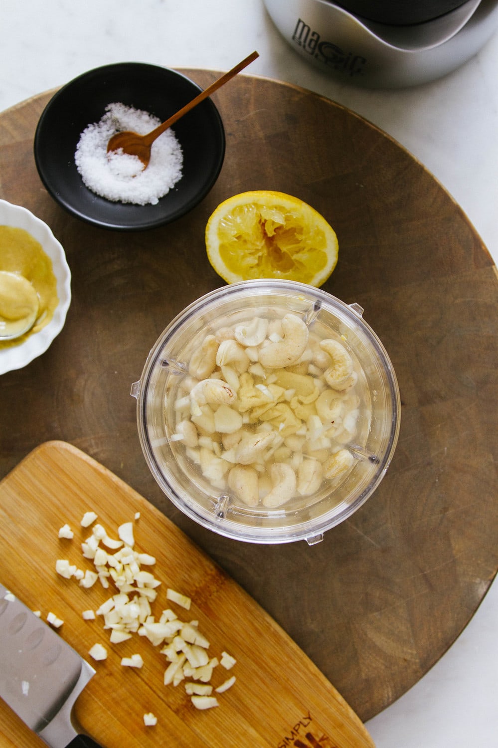 top down view of cashews soaking in water before making aioli, surrounded by minced garlic, dijon, salt and lemon halves