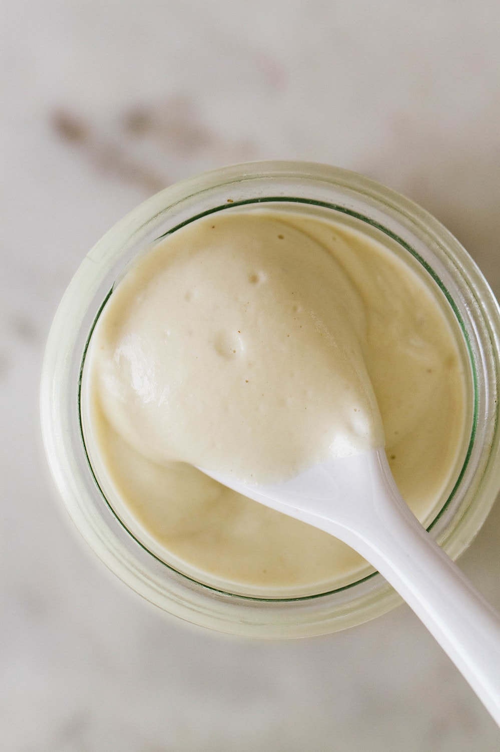 top down close up view of a spoon full of garlic vegan aioli sitting across a glass jar of aioli