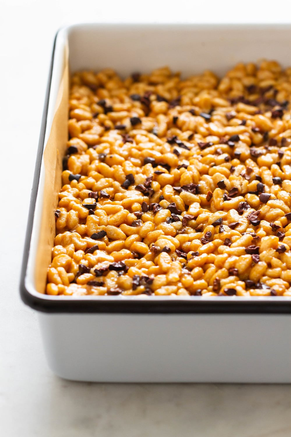 side angle view of peanut butter cacao nibs rice crispy treats pressed into a square white baking pan with black rim