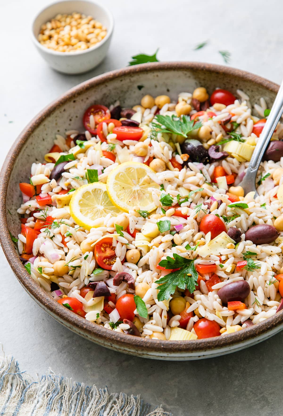 side angle view of vegan Mediterranean orzo salad in a large serving bowl with spoon.