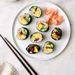 top down view of a plate full of sliced mango avocado cauliflower rice sushi rolls drizzled with spicy dynamite sauce.