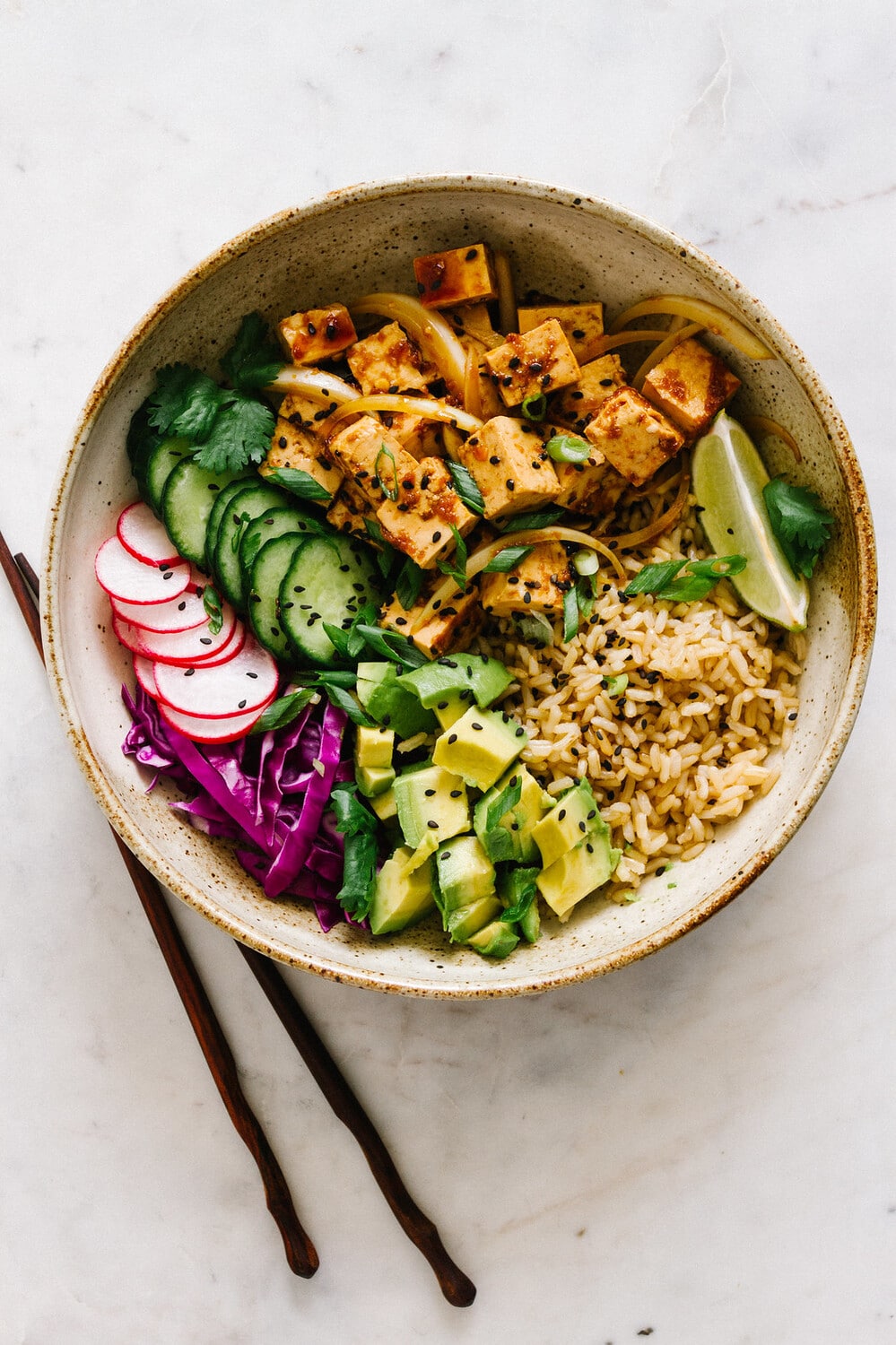 top down view of vegan poke bowl with tofu in a rustic bowl with chopsticks.