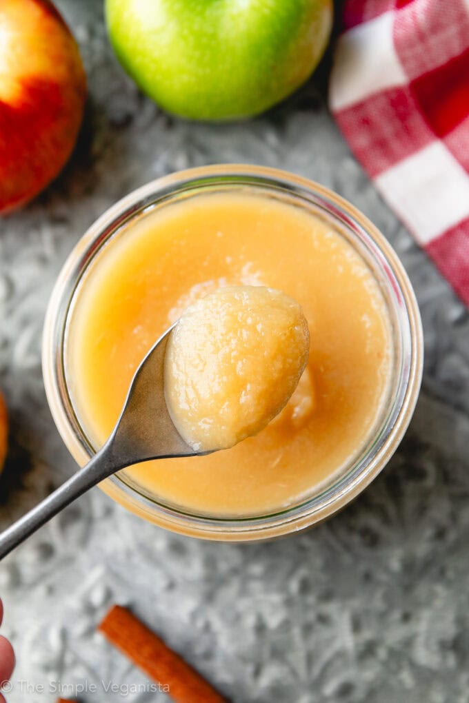 top down view of jar of fresh homemade applesauce with a spoon and items surrounding.
