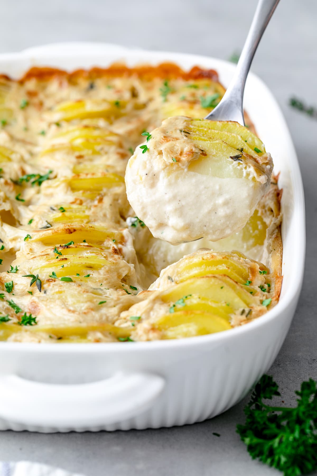 side angle view of vegan scalloped potatoes with serving spoon.