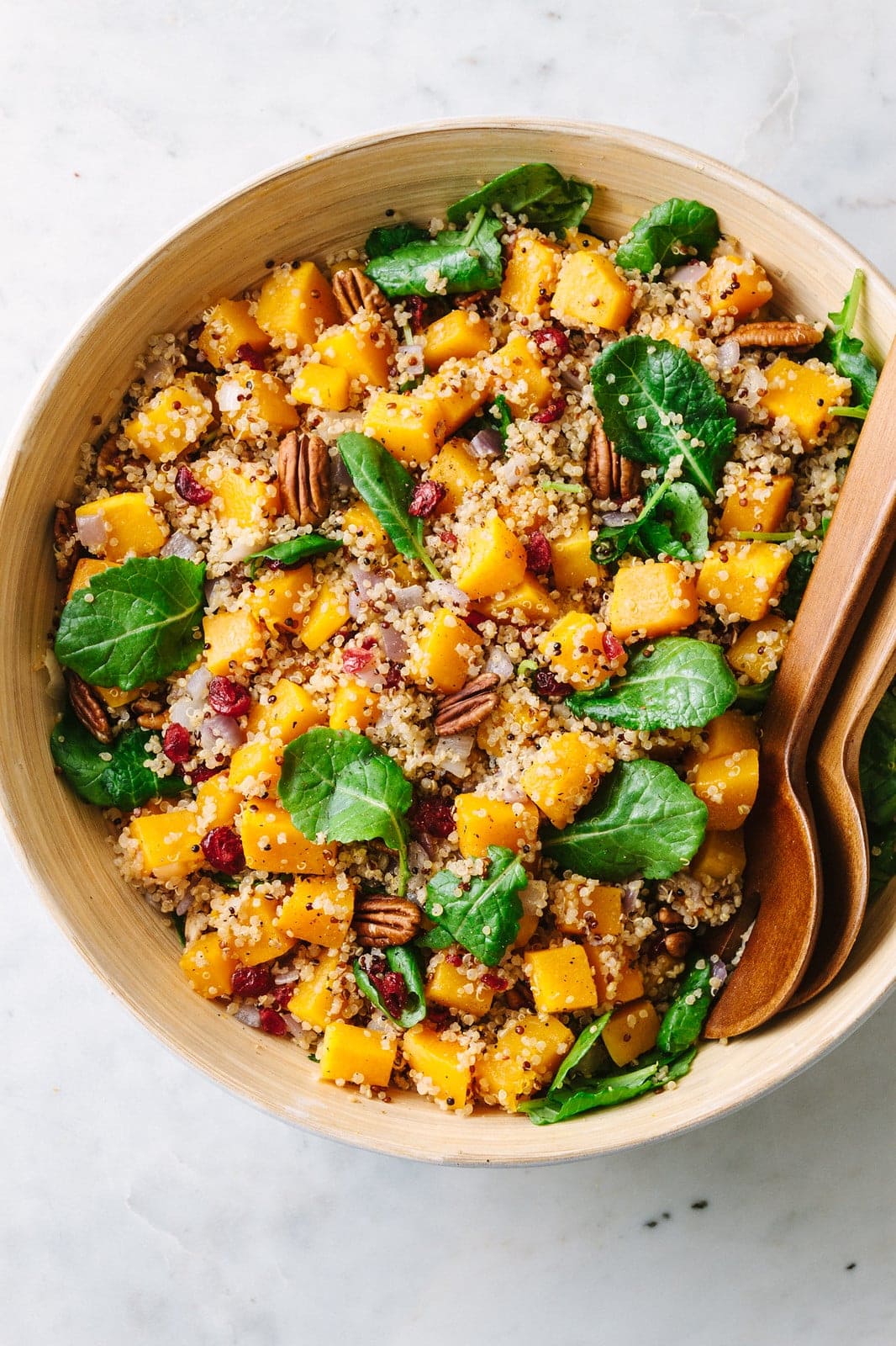 top down view of roasted butternut squash quinoa salad with pecans in a large serving bowl with wooden utensils.