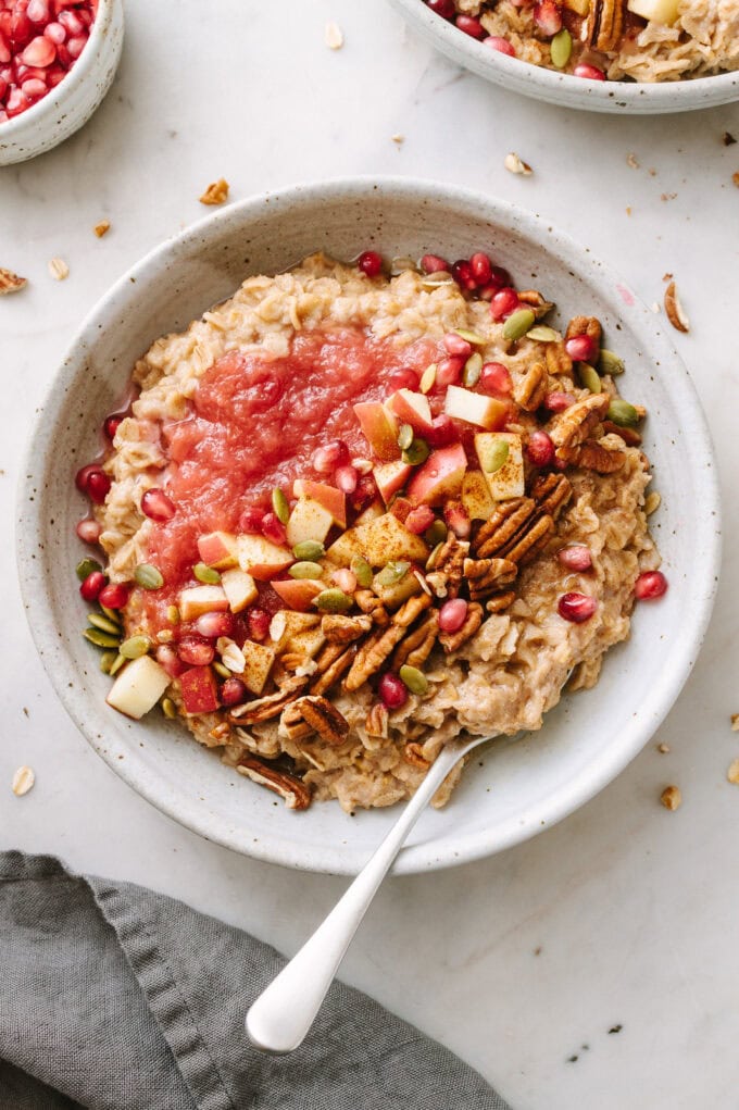 top down view of cinnamon oatmeal in a bowl with toppings and items surrounding.
