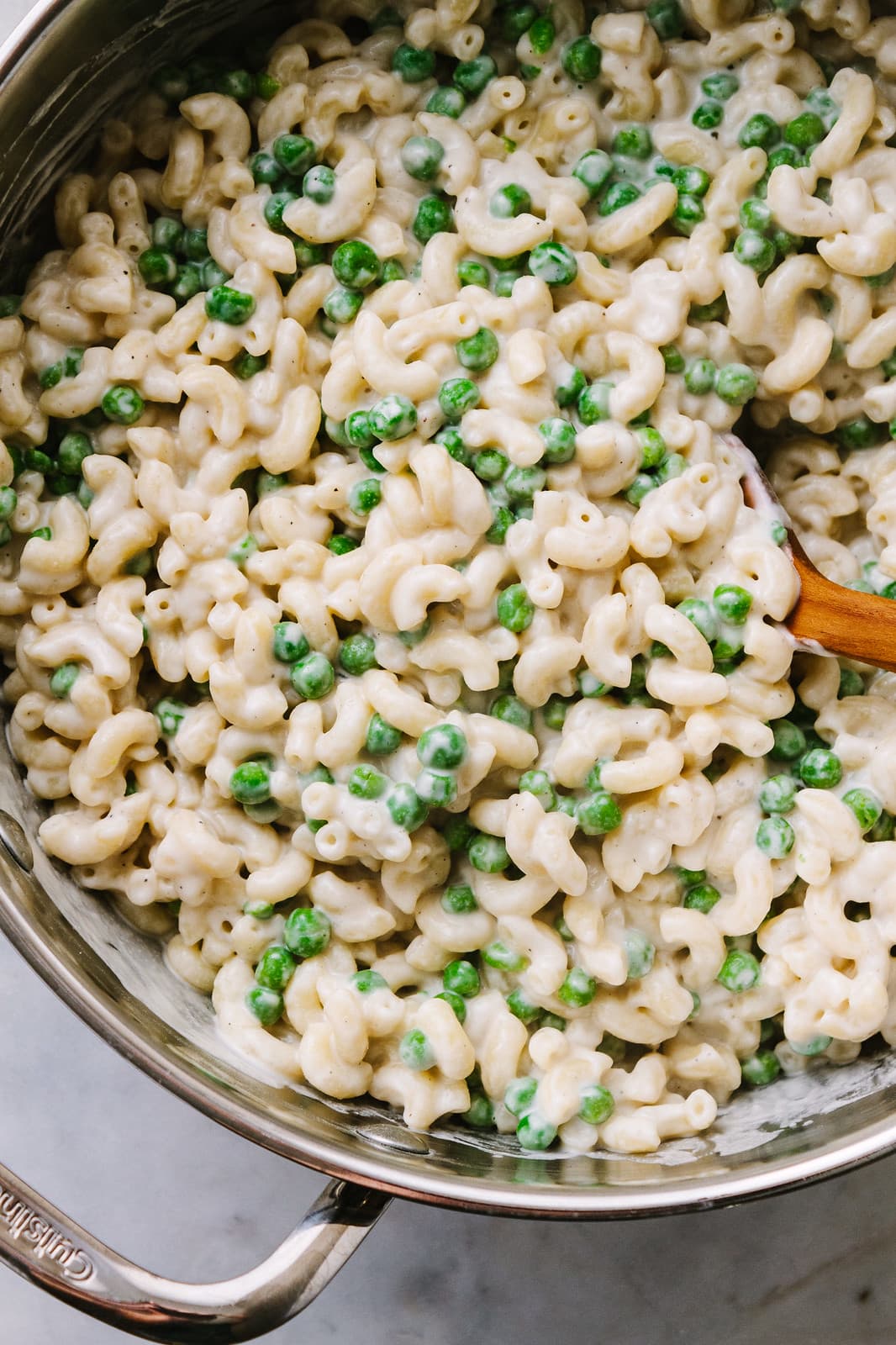 top down view of vegan mac and cheese with peas in a pot with wooden spoon.
