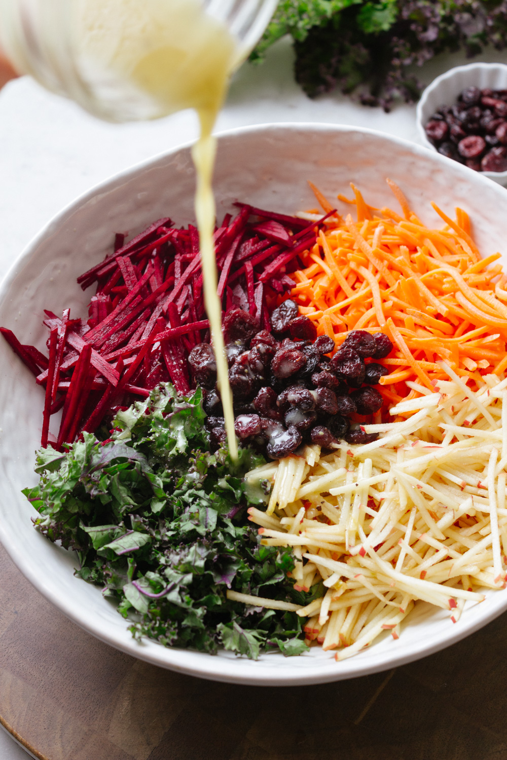 apple beet carrot kale salad being drizzled with orange dressing in white bowl