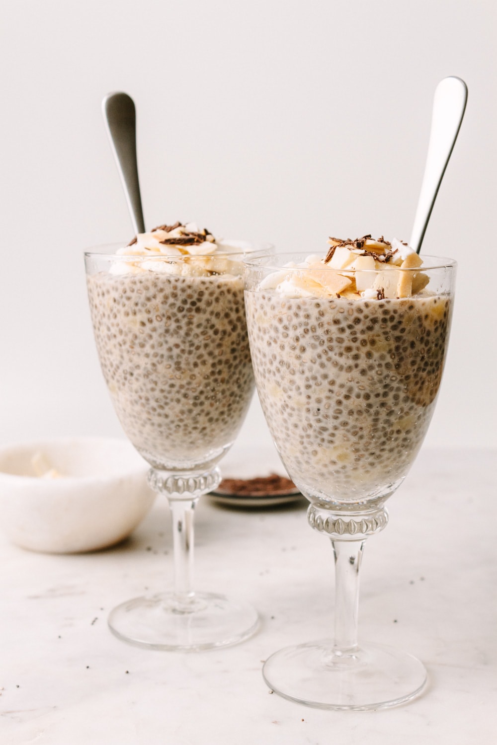 banana chia seed pudding in cup with banana slices, coconut flakes and shaved chocolate