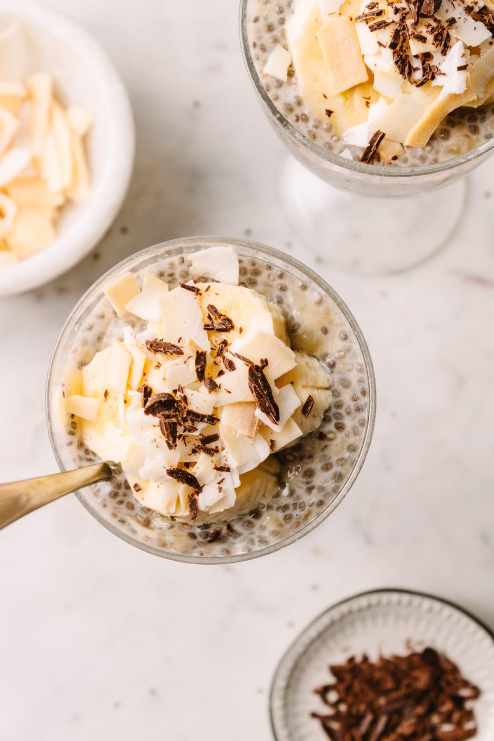 banana chia seed pudding in cup with banana slices, coconut flakes and shaved chocolate