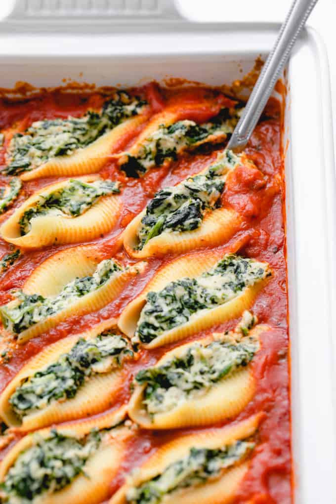 side angle view of spinach ricotta vegan stuffed shells in baking dish with serving spoon.